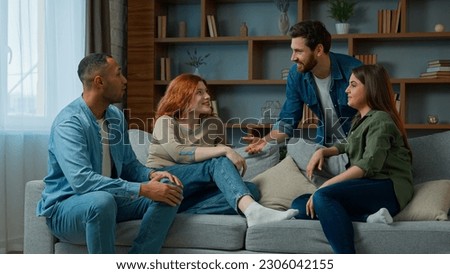 Four ethnic friends fellows companions sit on home couch talking discuss plans chatting friendly talk indoors gathered multiethnic men and women converse joking laughing sharing news real friendship