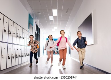 Four excited pupils with backpacks running corridor after lessons - Powered by Shutterstock