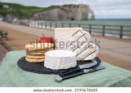 Four famous cheeses of Normandy, squared pont l'eveque, camembert cheese, yellow livarot, heartshaped neufchatel and view on promenade and alebaster cliffs Porte d'Aval in Etretat, Normandy, France