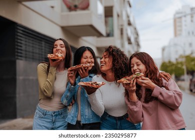 Four female multiethnic girlfriends eating slices of pizza and laughing on the streets