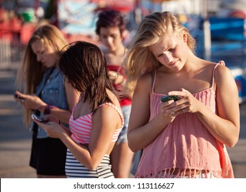 Four female teenagers using their phones outside