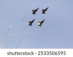 Four fighter jets performing an aerial display with flares against a clear blue sky.