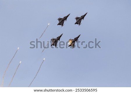 Four fighter jets performing an aerial display with flares against a clear blue sky.