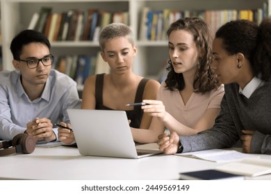 Four focused multiethnic students do homework together sit in library, discuss online task use laptop, prepare for exams, search information on internet, share ideas, work on group project. Education - Powered by Shutterstock