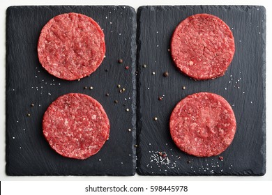 Four Fresh Raw Prime Black Angus Beef Burger Patties On Black Stone Plates. Top View.