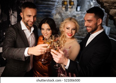 Four friends with champagne glasses celebrating and toasting in restaurant