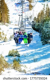 Four Friends Children Sit High Together On Chairlift Lifting On The Mountain With Green Forest Below