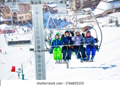 Four Friends Children Sit Together On Chairlift Lifting On The Mountain With Crowded Slope And Station Below