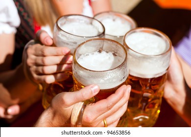 Four friends with a fresh beer in a Beer garden; close-up on beer stein - Shutterstock ID 94653856