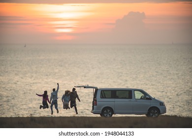 The four friends have fun near the minivan against the sunset sky
