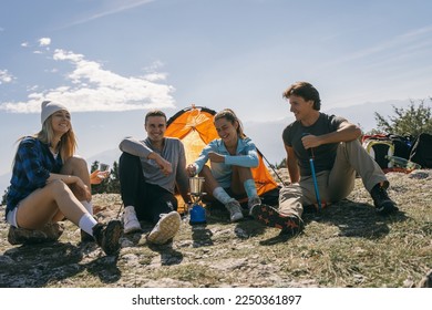 Four friends having fun while making coffee and sitting at the top of the mountain