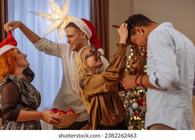 Four friends having a great time hanging out during Christmas Eve while putting on props like Santa hat, glasses and others - Powered by Shutterstock