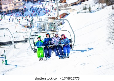 Four Friends Kids Sit Together On Chairlift Lifting On The Mountain With Crowded Slope And Station Below