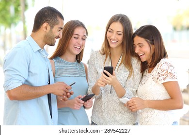 Four friends laughing happy and watching social media in a smart phone in the street every one with his own phone