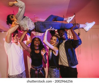 Four friends lifting a woman over their heads horizontally up to the ceiling at a house party. Young men and women having fun at a colorful house party. - Powered by Shutterstock