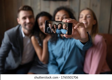 Four friends making selfie, photo on smart phone screen view, focus on hand holds device. Modern tech usage, have fun party event hanging out, taking memory pic, multi ethnic people friendship concept - Powered by Shutterstock