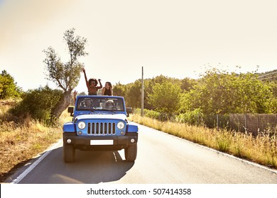 Four friends on the road in open car, two women standing