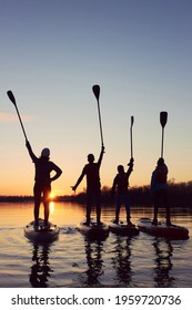 Four Friends On Stand Up Paddle Board (SUP) On A Flat Quiet Winter River At Sunset Raising His Paddles Up