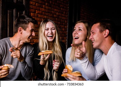 Four friends sitting at a table in the cafe and eat pizza on brick wall background - Shutterstock ID 733834363