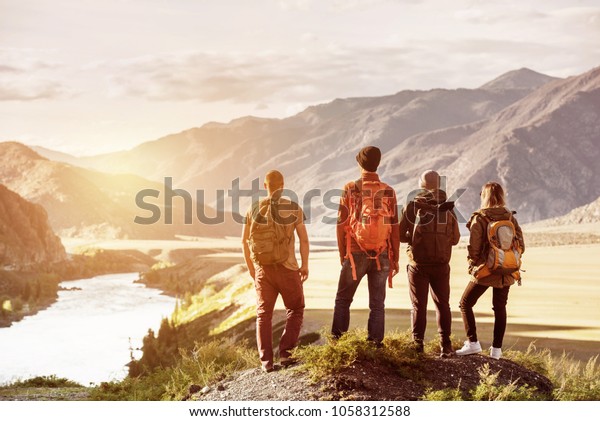 Four\
friends stands on view point and looking at sunset mountains and\
river. Adventures travel concept with space for\
text