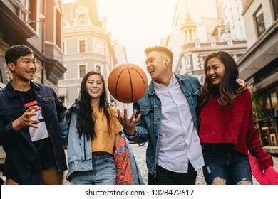 Four friends walking together on the street, with women holding skateboards and man holding basketball. Asian men and women outdoors on city street. - Shutterstock ID 1328472617