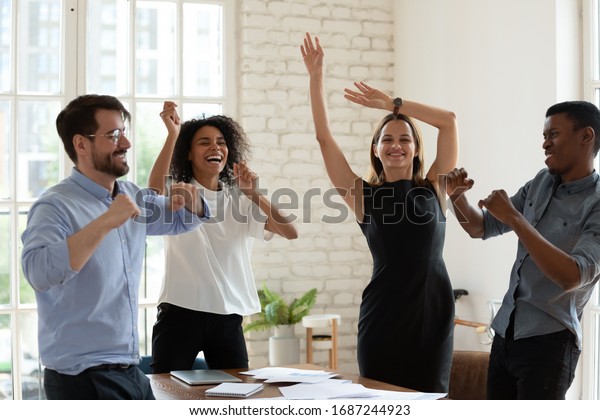 Four funny active multi-ethnic business team\
staff members dancing moving listening music gathered in office\
board room. Succeed common goal feels happy, corporate holiday\
event celebration concept