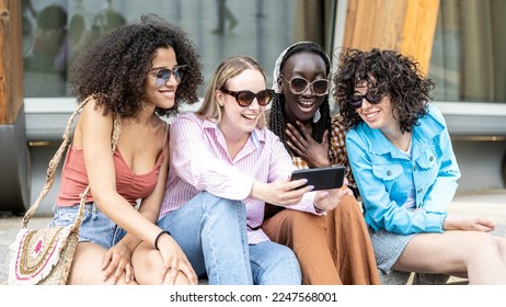 Four girls teenagers of Generation Z in the city, young women sitting on a bench in the city and using smart phone for social network - Powered by Shutterstock