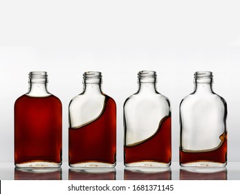 Four glass bottles in a row with different amount of brown color beverage cognac in each, that churning and spills out.