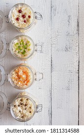 Four Glass Jars Full Of Homemade Fermented Cabbage With Carrot, Scallions, Black Pepper And Cranberries On Vertical Wooden White Background. Flat Lay With Healthy Vegetarian Food Concept. Copy Space. 