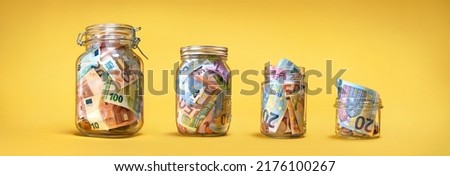 Four glass jars with savings, cash money (euro banknotes) banknotes) on yellow background