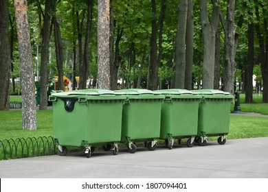 Four green trash cans on the wheels in the park. Recycled garbage, bins, waste. Ecological mission, save the planet from danger pollution