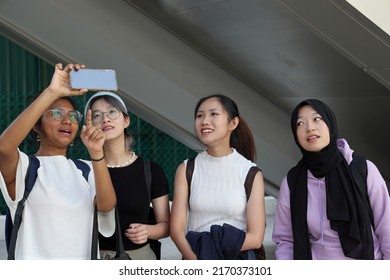 Four group young attractive Asian multi ethnic woman friends colleagues students talk walk discuss mingle outdoors backpack handphone photo