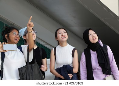 Four group young attractive Asian multi ethnic woman friends colleagues students talk walk discuss mingle outdoors backpack handphone photo show point
