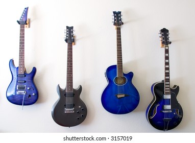 Four Guitars Hanging On White Painted Wall