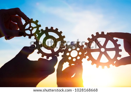 Four hands of businessmen collect gear from the gears of the details of puzzles. against the background of sunlight. The concept of a business idea. Teamwork. strategy. cooperation