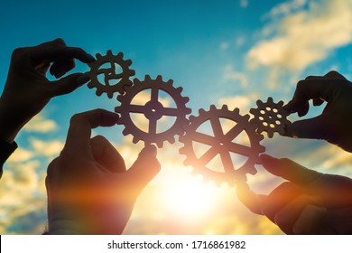 Four hands of businessmen connect gears to a puzzle on a background of sunset. Business concept idea, partnership, cooperation, teamwork, community, creative