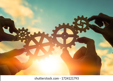 Four hands of businessmen connect gears to a puzzle on a background of sunset. Business concept idea, partnership, cooperation, teamwork, community, creative