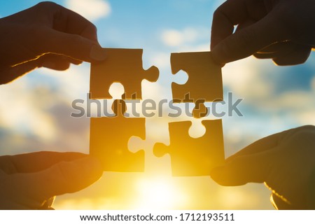 Four hands of businessmen connect puzzle pieces into a single unit on a sunset background. Business concept idea, teamwork, cooperation, partnership, creative