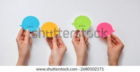 Four hands hold speech bubbles with dots, symbolizing dialogue, correspondence, social interaction, and the exchange of ideas.