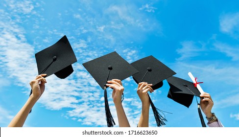 Four hands holding graduation hats on background of blue sky.