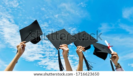 Four hands holding graduation hats on background of blue sky.