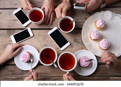 Four hands with smart phones holding  cups with tea, on wooden table background - Shutterstock ID 344092670