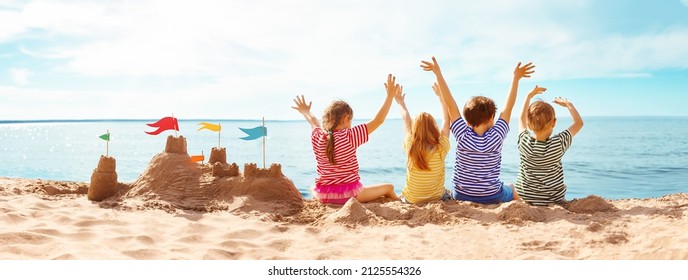 Four happy children sitting onthe sea coast and raising up their hands. Concept of the friendship and vacation. - Powered by Shutterstock