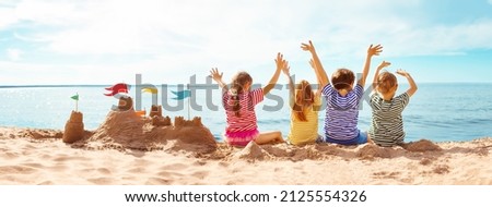 Four happy children sitting onthe sea coast and raising up their hands. Concept of the friendship and vacation.