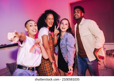 Four happy friends having a good time at a house party. Vibrant young people celebrating while standing in bright neon light. Group of multicultural friends enjoying their weekend together.
