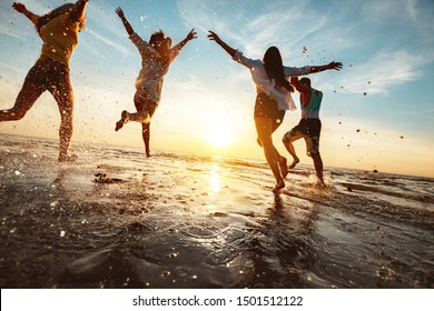 Vier fröhliche Freunde bei Sonnenuntergang Beach Party läuft auf Wasser