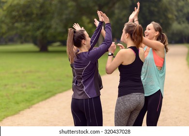 Four Happy Healthy Women Giving Double High Five Gesture While Relaxing After An Outdoor Exercise At The Park.