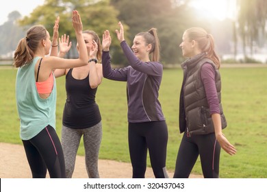 Four Happy Healthy Women Giving Double High Five Gesture While Relaxing After An Outdoor Exercise At The Park.