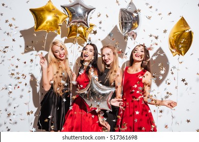 Four happy joyful young women with star shaped balloons and confetti having party over white background