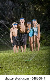 Four Happy Kids Standing Arm In Arm Shouting And Laughing, Soaked By Lawn Sprinkler